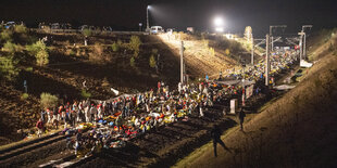 Es ist Nacht und viele Menschen stehen auf oder um ein Bahngleis