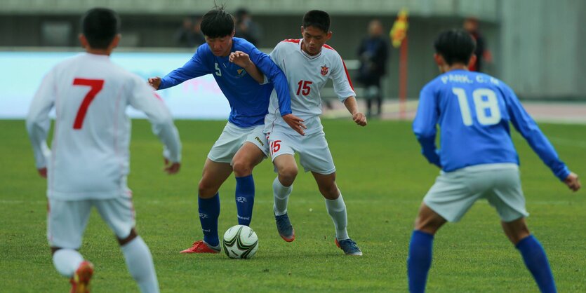 Junge Fußballer in weißen und blauen Trikots kämpfen auf dem grünen Spielfeld um den Ball