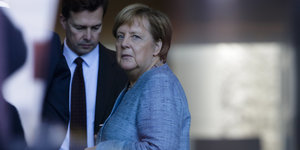Angela Merkel trägt einen himmelblauen Blazer und guckt über ihre linke Schulter