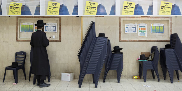 Ein ultraorthodoxer Jude steht in einem Gebäude an einer Wand mit Wahlplakaten