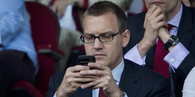 Ein Mann benutzt sein Handy auf der Tribüne bei einem Fußballspiel