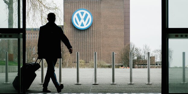 Ein Mann geht durch eine Eingangstür, in der Ferne steht ein VW-Werk.