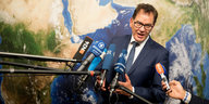 Entwicklungsminister Müller steht vor einer Weltkarte und spricht in Mikrofone.