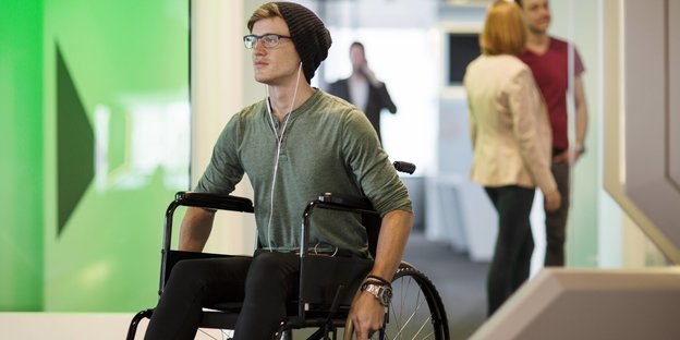 Ein junger Mann mit Mütze fährt im Rollstuhl durch ein Büro