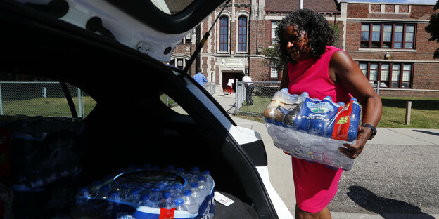 Eine Frau trägt in Plastik eingeschweißte Wasserflaschen in einen Kofferraum