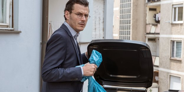 Ein Mann wirft eine blaue tüte in den Müll