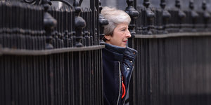 Theresa May tritt zwischen den Gittern eines Zauns hervor