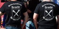 die Rücken zweier Männer, auf ihren T-Shirts steht: „Sicherheitsdienst Arische Bruderschaft“