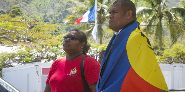 Ein Mann, in einer Fahne von Neukaledonien gehüllt, steht zusammen mit einer Frau in der Nähe eines Wahllokales