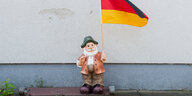 Ein Gartenzwerg steht vor einer Hauswand, in der Hand hält er eine Deutschlandflagge