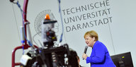 Merkel steht in veilchenblauem Jacket vor einem Roboter