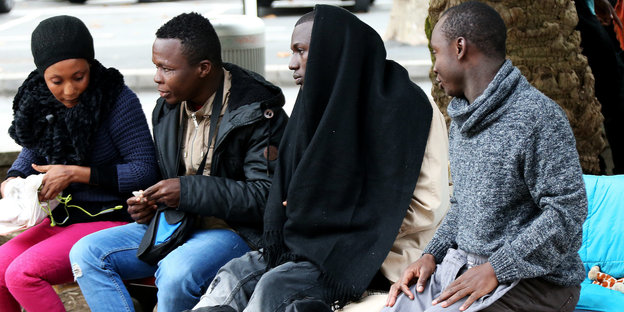 Migranten sitzen auf einer Bank an einem Platz in Bayonne