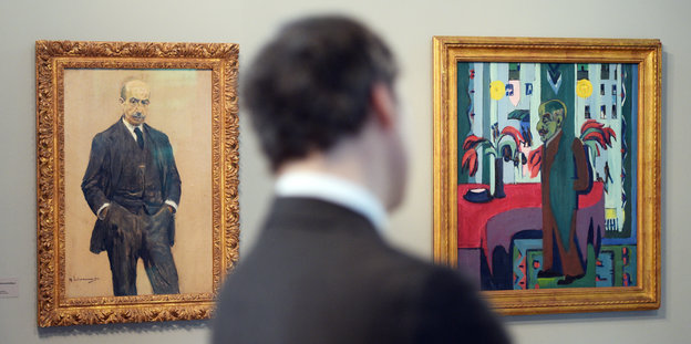 Hinterkopf eines braunhaarigen Mannes vor zwei bunten Bildern in einer Ausstellung.