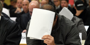 Ein Angeklagter hält ein Blatt Papier vor sein Gesicht