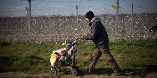 Ein Mann schiebt einen Kinderwagen. Hinter ihm ist ein Stacheldrahtzaun zu sehen