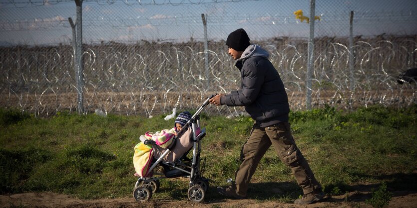 Ein Mann schiebt einen Kinderwagen. Hinter ihm ist ein Stacheldrahtzaun zu sehen