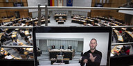 Auf einem Bildschirm ist ein Mann zu sehen, der in Gebärdensprache spricht. Im Hintergrund ist der Plenarsaal des Berliner Abgeordnetenhauses zu sehen