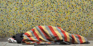 Obdachloser liegt in einen Decke eingewickelt auf dem Boden