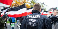 Ein Polizist vor einem Demonstrationszug mit schwarz.weiß-roten Fahnen