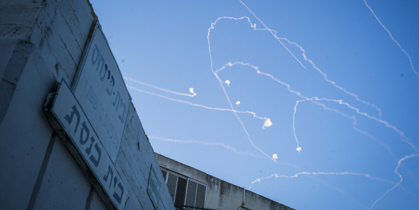 Ein Gebäude mit hebräischer Aufschrift, am Himmel sind leuchtende Geschosse zu sehen