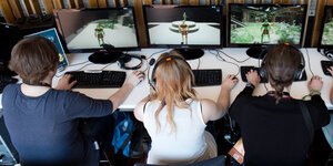 Frauen und Männer sitzen mit Kopfhörern vor Computern und spielen ein Videospiel