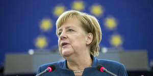 Merkel steht am Rednerpult, im Hintergrund ist die EU-Flagge. Die Sterne stehen über ihrem Kopf und sehen aus wie ein Heiligenschein