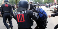 Ein Polizist schlägt mit einem Schlagstock auf einen schwarzgekleideten Demonstranten