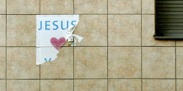Ein zerflettertes Plakat klebt an einer Wand. Jesus steht drauf. Der Rest ist abgerissen.
