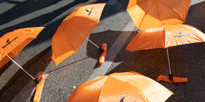 orangene Regenschirme liegen auf der Straße - es ist eine Protestaktion bei einer Seebrücken-Demo