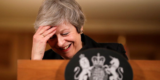 Theresa May lacht und stützt ihren Kopf in die Hand