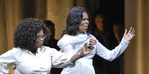 Oprah Winfrey und Michelle Obama halten sich an der Hand und ziehen Grimassen