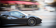Ein schwarzer Ferrari fährt auf einer Straße, der Hintergrund ist verschwommen
