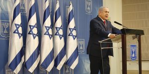 Benjamin Netanjahu, Israels Ministerpräsident, steht neben Israel-Fahnen an einem Pult