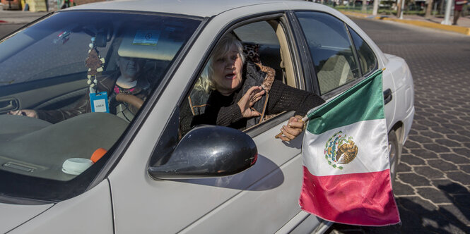 Eine Frau hält eine mexikanische Flagge aus dem Auto