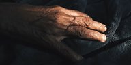 Eine Hand eines alten Menschen liegt auf einer schwarzen Decke
