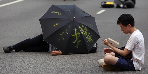 Ein Mensch sitzt auf der Straße, ein anderer liegt unter einem Regenschirm