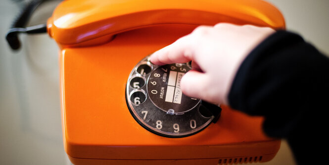 Ein Finger bedient ein oranges Wählscheibentelefon