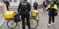 Ein Polizeibeamter legt Hand am Fahrrad einer Postzustellerin an.