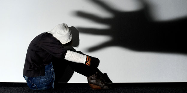 Ein Mädchen sitzt vor einer Wand in Hannover, auf der der Schatten einer Hand groß zu sehen ist