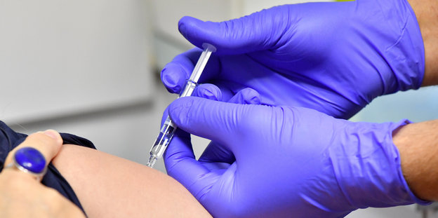 Eine Person trägt blaue Gummihandschuhe und verabreicht eine Impfung
