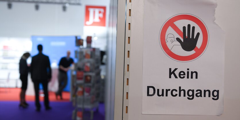 Im Vordergrund warnt ein "Kein-Durchgang"-Schild vor dem Passieren, im Hintergrund stehen Menschen vor einem Messestand der rechten Zeitung Junge Freiheit