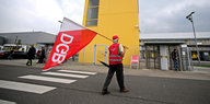Ein Mann in einer roten Weste steht während eines Streiks bei Amazon mit einer DGB-Flagge vor dem Unternehmensstandort in Leipzig