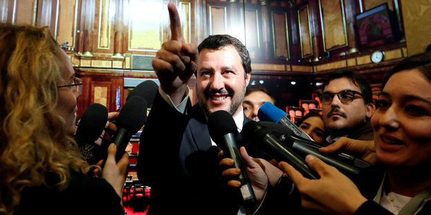 Matteo Salvini zeigt mit dem Finger. Um ihn herum stehen zahlreiche Reporter