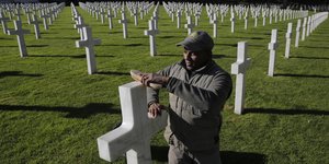 Ein Mann reinigt ein Kreuz auf einem Soldatenfriedhof