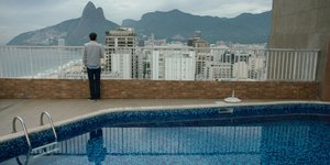 Ein Mann steht hinter einem Pool und guckt von der Veranda auf ein Stadtpanorama