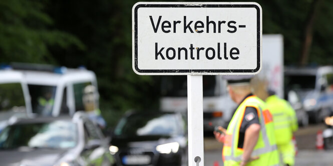 Ein Polizist steht neben einem Schild mit der Aufschrift: "Verkehrskontrolle".