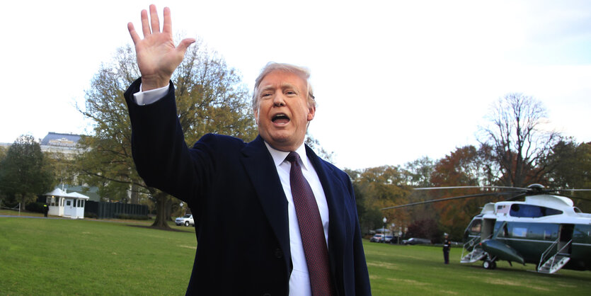 Donald Trump, Präsident der USA, winkt. Im Hintergrund ein Helikopter auf grüner Wiese.