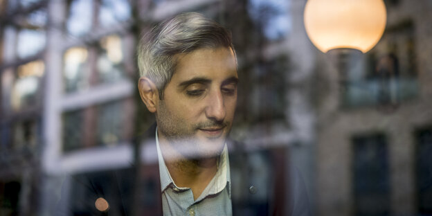 Michel Abdollahi durch eine Fensterscheibe mit Spiegelungen gesehen