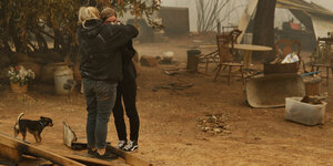 Zwei Frauen umarmen sich weinend, im Hintergrund die Trümmer ihres vom kalifornischen Waldbrand zerstörten Hauses
