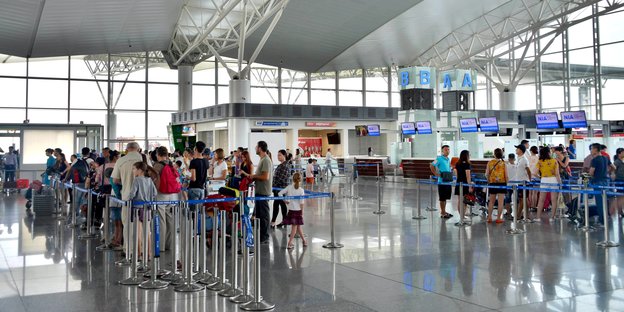 Ansicht des Inneren eines Flughafenterminals, einige Reisende stehen in einer Schlange zwischen Absperrungen